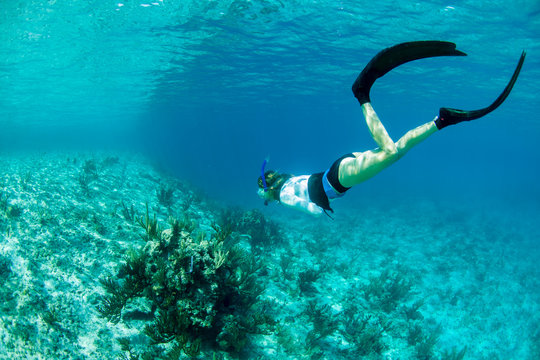 Woman snorkeling above a coral reef in clear blue water near Staniel Cay, Exuma, Bahamas.
