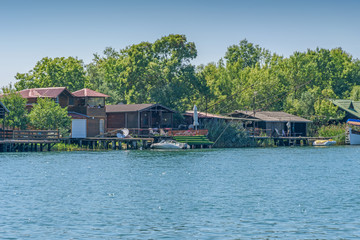 Fototapeta na wymiar River Bojana and small wooden houses with marinas and boats on the riverbank for tourists. Water landscape