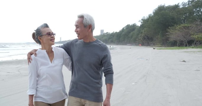 Asian senior couple walking and talking on beautiful tropical beach in slow motion.
