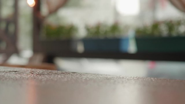 Rainy day in summer cafe with terrace. Raindrops falling on the wood table surface and splashing, closeup view. Wet table with water from rain.