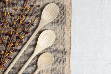 cooking concept with wooden spoons and berry twigs laying on two thirds burlap and one third linen...