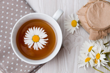 Obraz na płótnie Canvas cup of tea and camomile and jar on a polka dot fabric tea can lace grey brown orange beige fliwers
