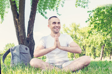 Naklejka na ściany i meble Happy man sitting in Park in summer, man meditates, guy holding hands in namaste gesture, portrait, toned