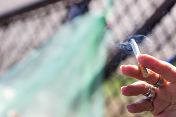 Blurred image, Soft focus Cigarette in women hand with smoke in the park, Hand with burning cigarette and smoking.