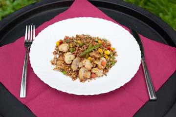 Buckwheat porridge with mushrooms and vegetables on a plate. Served table with knife and fork.