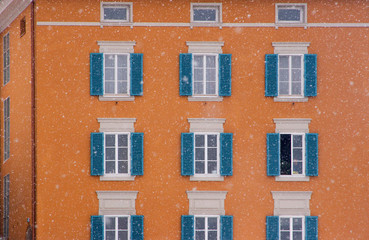 Fototapeta na wymiar Austria, Salzburg. Blue shutters on orange apartment building in snowfall. (UNESCO World Heritage Site)