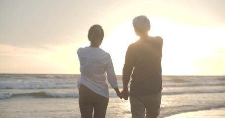 Asian senior couple walking and talking on beautiful tropical beach in slow motion. - Powered by Adobe