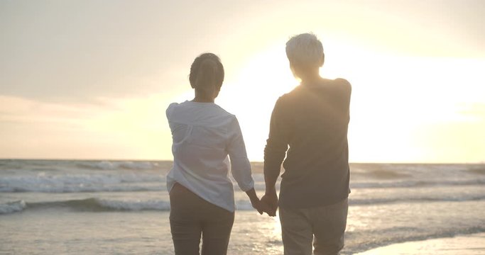 Asian Senior Couple Walking And Talking On Beautiful Tropical Beach In Slow Motion.