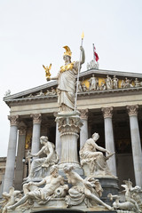 Fototapeta premium Austria, Vienna. A romanesque statue stands on a dry water feature in front of a building with columns.