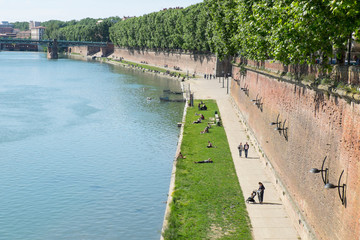 Fototapeta premium France, Toulouse, near the Pont Neuf bridge, Henri Martin promenade adjacent to the Garonne River, young couples share time together and individuals lie in the sun looking at their cell phones.