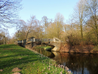 Fototapeta na wymiar Stone bridge over canal in park. Spring