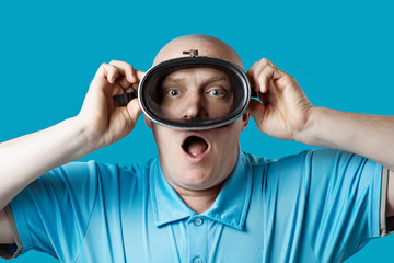 bald brutal man in a diving mask holds his breath on blue background