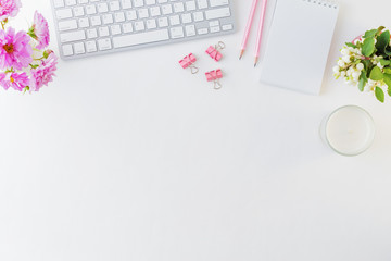 Flat lay blogger or freelancer workspace with a notebook, keyboard and pink flowers on a white background