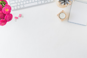 Flat lay blogger or freelancer workspace with a notebook, keyboard and pink flowers on a white background