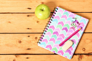 Pink notebook and apple on wooden background