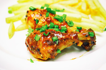 Chicken legs with french fries potatoes in a white plate