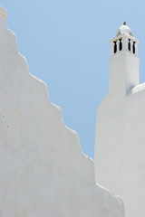 Greece, Mykonos, Hora. Whitechurch belfry against light blue sky and irregular wall.