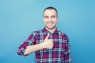 Portrait, smiling young man in casual clothes, shows thumb up, looking at camera, blue background, copy space, for advertising, slogan