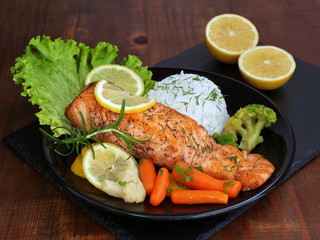 Grilled salmon fillet with  rice and vegetables on black plate over dark wooden table