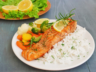 Grilled salmon fillet with vegetables, rice and rosemary on white plateover wooden table