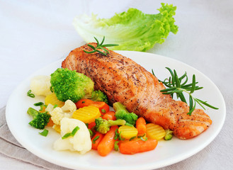 Grilled salmon fillet with vegetables lemon and rosemary over white plate