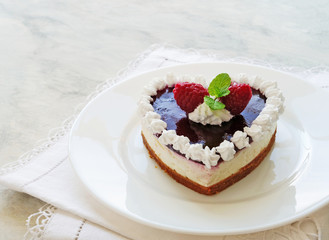 Heart shaped no-bake cheesecake with graham cracker crust, cream cheese filling and raspberry jelly, decorated with whipped cream on white plate.