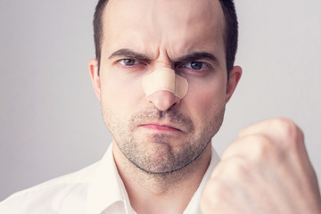 Angry man with the broken nose threatens with a fist, gray background