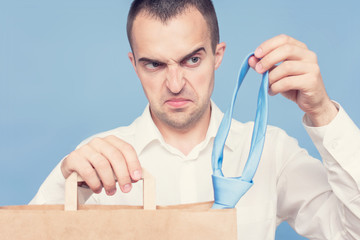 Portrait. Dissatisfied man in a white shirt with package purchases, man pulls out his tie, close up, cropped image, toned