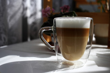 Delicious aromatic morning coffee in a glass mug with double walls on a windowsill against a curtain