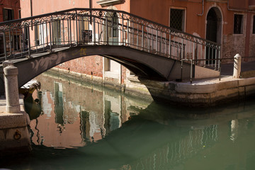 Fototapeta na wymiar Italy, Venice. Sunlight slips in between buildings to illuminate walls and create reflections in quiet canal waters.