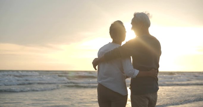 Asian senior couple embracing each other on the beach at sunset in slow motion.