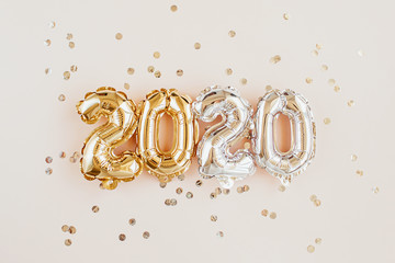 New year 2020 celebration. Gold and silver foil balloons numeral 2020 and confetti on pink...