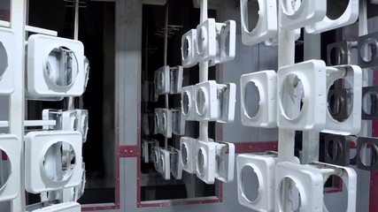 line for painting metal products in white color coating. Square metal products with a round hole hang on mounts after powder painting