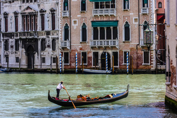 Fototapeta na wymiar Venice, Italy. Gondolier steers his shiny, black gondola through a canal near Venetian palaces