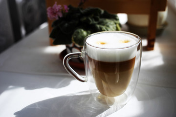 Delicious aromatic morning coffee in a glass mug with double walls on a windowsill against a curtain