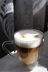 Delicious aromatic morning coffee in a glass mug with double walls on a windowsill against a curtain