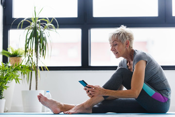 Senior woman using smartphone at home after exercise. The use of technology by the elderly.