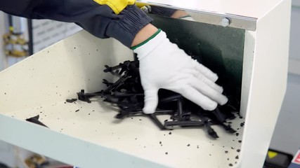 man in white gloves puts plastic pieces in a shredder for grinding and recycling of plastic waste