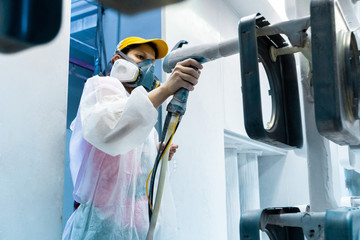 Powder coating of metal parts. A woman in a protective suit sprays white powder paint from a gun on metal products