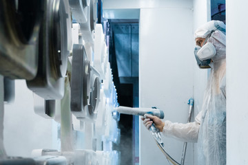 Powder coating of metal parts. Man in a protective suit sprays white powder paint from a gun on metal products