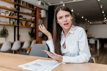 confused woman in the office with phone and papers