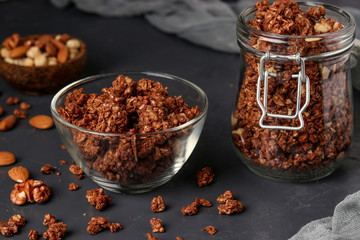 Granola crispy muesli with natural honey, chocolate and nuts in a glass jar and bowl against a dark background, healthy food, horizontal orientation