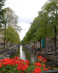 Fototapeta na wymiar Red flowers top a bridge crossing a boat lined canal