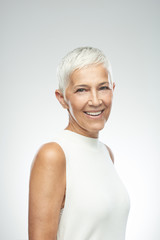 Beautiful smiling senior woman with short gray hair posing in front of gray background. Beauty...