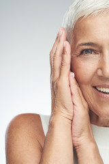 Beautiful smiling senior woman with short gray hair posing in front of gray background. Beauty photography.