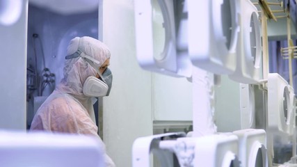 Powder coating of metal parts. Man in protective suit sprays white powder paint from gun on metal products