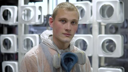Portrait of a man in a mask in the paint shop. He is wearing a protective mask and a protective robe, he looks at the camera