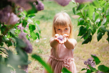 Beautiful little girl giving lilac flowers bouquet in park outdoors