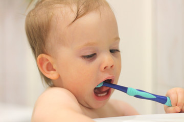 cute little white child with a tail brushes his teeth near the washbasin