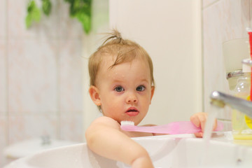 cute little white child with a tail brushes his teeth near the washbasin